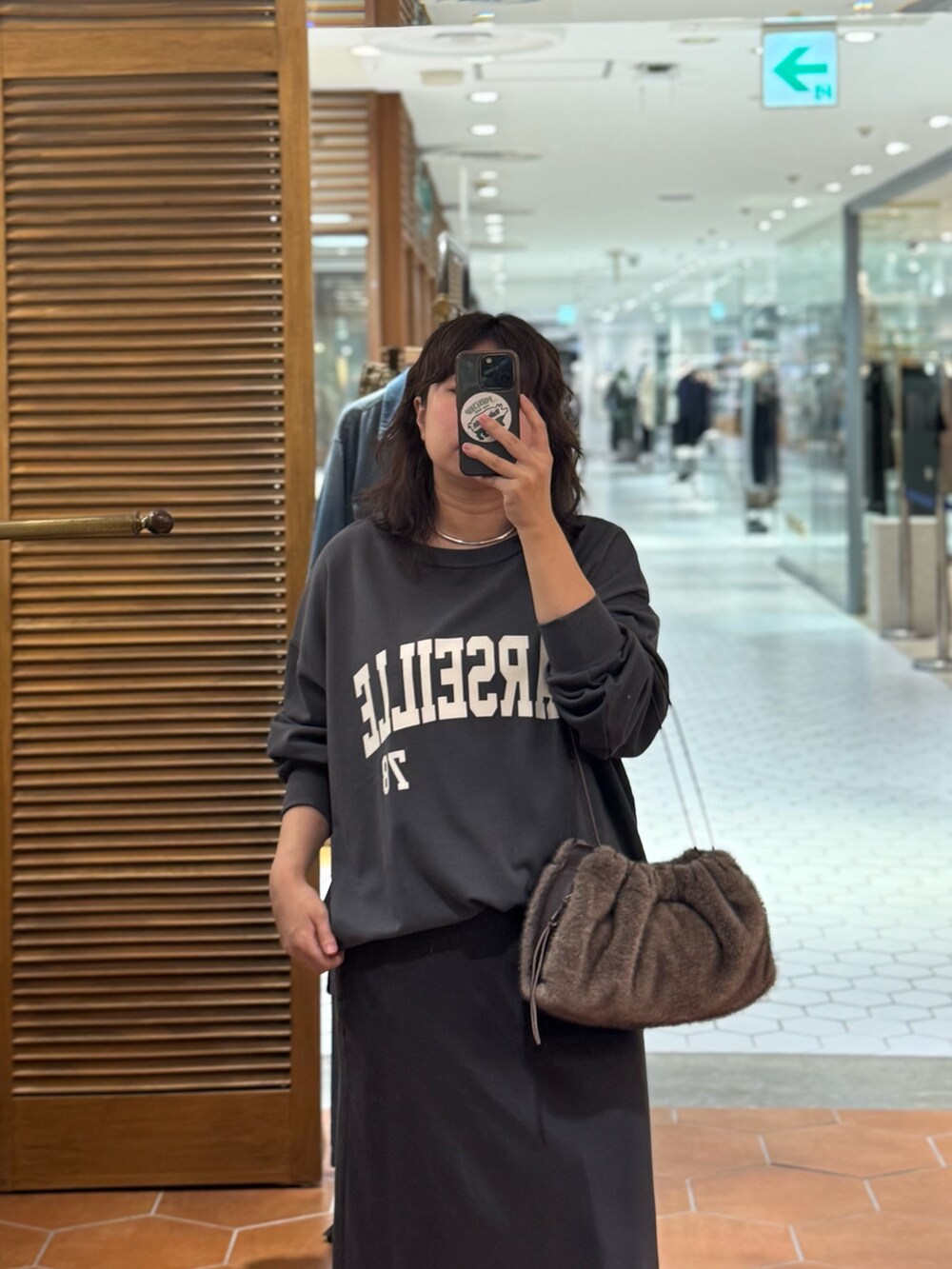 グレー系のスカート、ブラウン系のハンドバッグ、グレー系のスウェットを着用したレディースの秋コーディネートの3枚目の写真