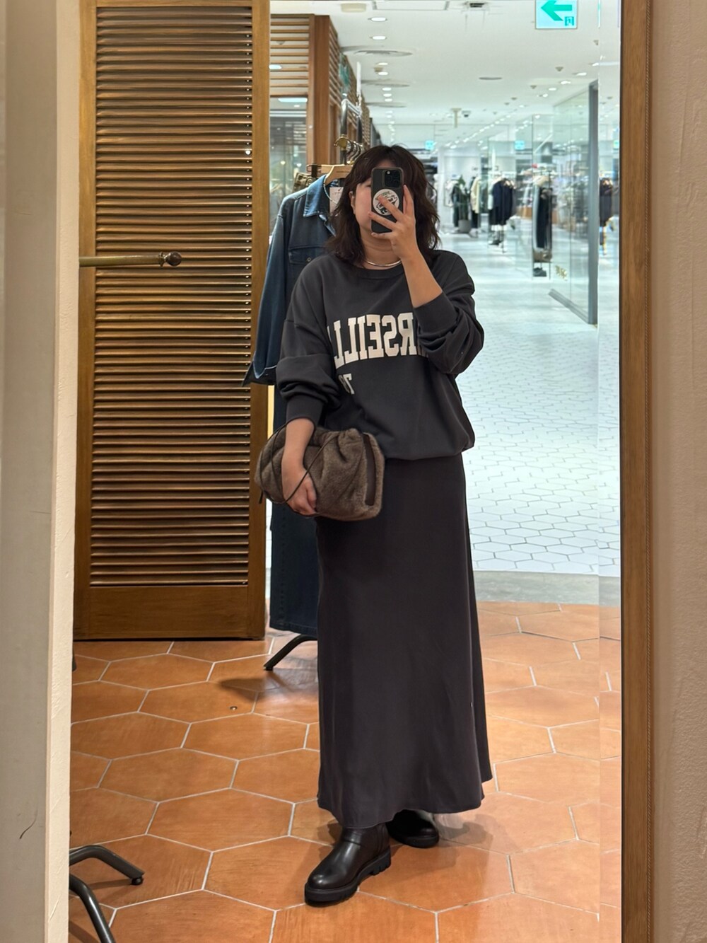 グレー系のスカート、ブラウン系のハンドバッグ、グレー系のスウェットを着用したレディースの秋コーディネートの2枚目の写真