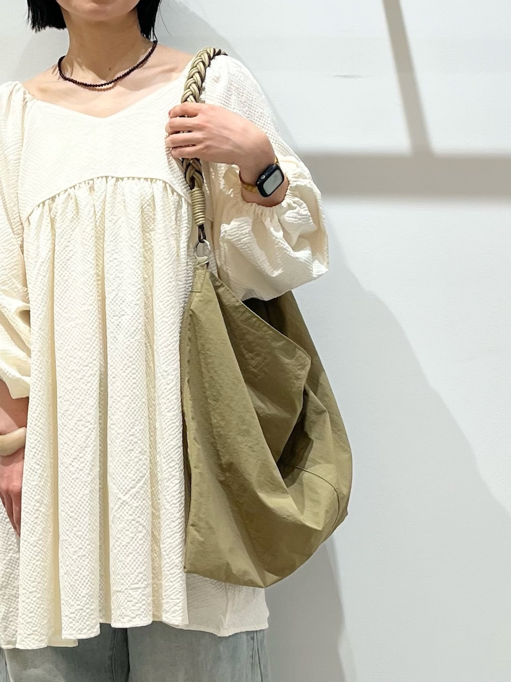グリーン系のショルダーバッグ、ホワイト系のワンピース、ブルー系のデニムパンツを着用したレディースの春コーディネートの4枚目の写真