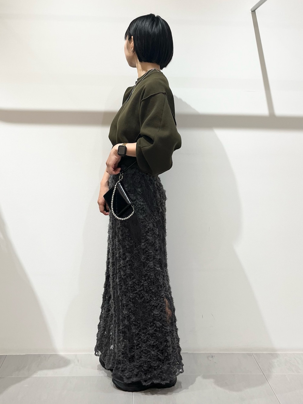 グリーン系のニット/セーター、ブラック系のブーツ、グレー系のスカートを着用したレディースの秋コーディネートの2枚目の写真