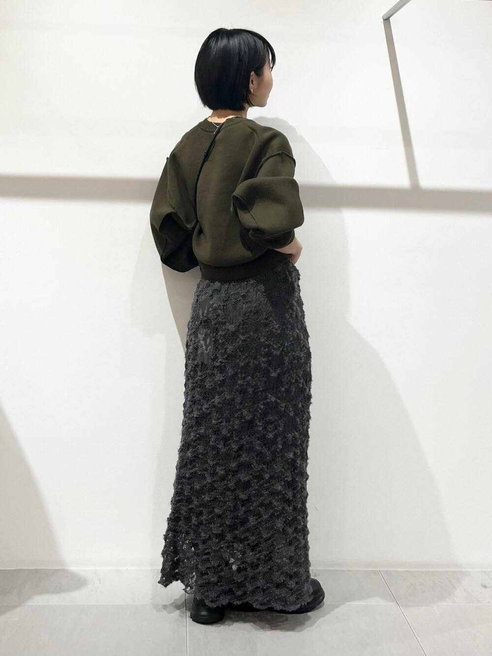 グリーン系のニット/セーター、ブラック系のブーツ、グレー系のスカートを着用したレディースの秋コーディネートの3枚目の写真