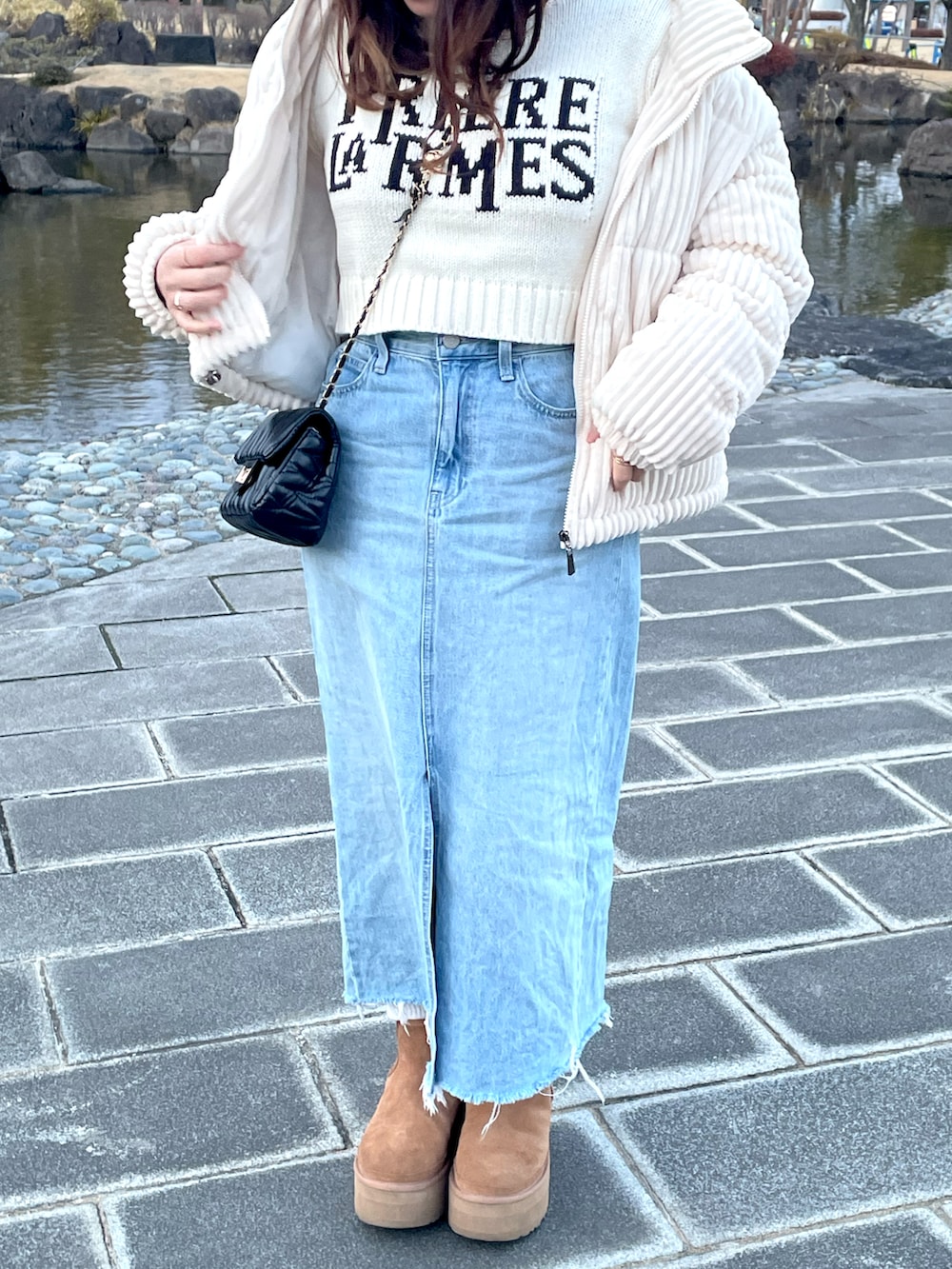 ブルー系のデニムスカート、ブラウン系のブーツ、ホワイト系のニット/セーターを着用したレディースの春コーディネートの2枚目の写真