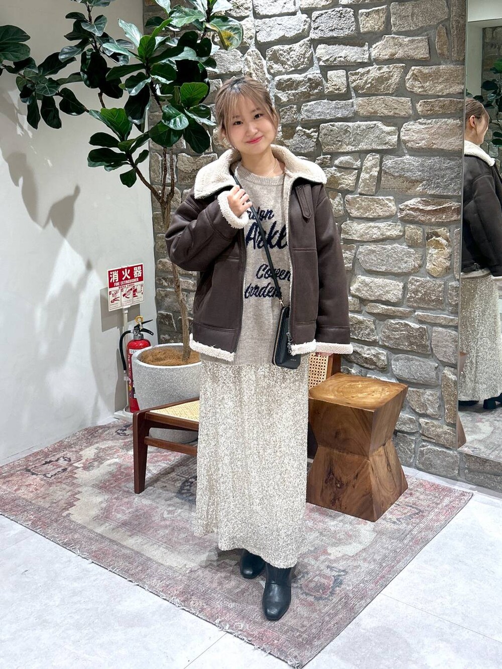 ブラック系のブーツ、ベージュ系のスカート、ブラウン系のムートンコートを着用したレディースの秋コーディネートの2枚目の写真