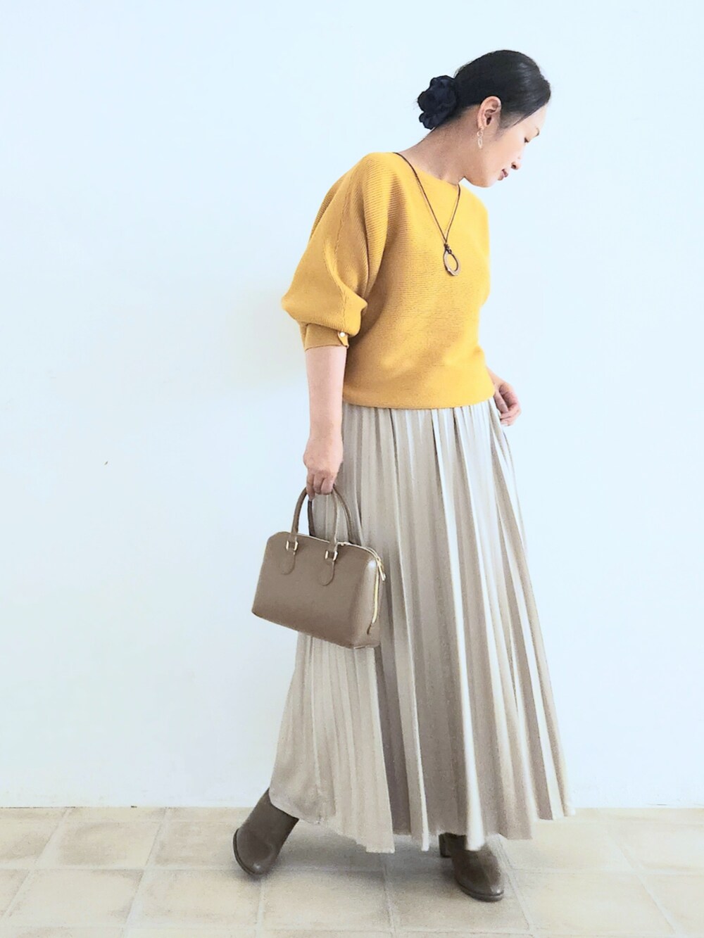 ベージュ系のスカート、ブラウン系のブーツ、イエロー系のニット/セーターを着用したレディースの秋コーディネートの2枚目の写真