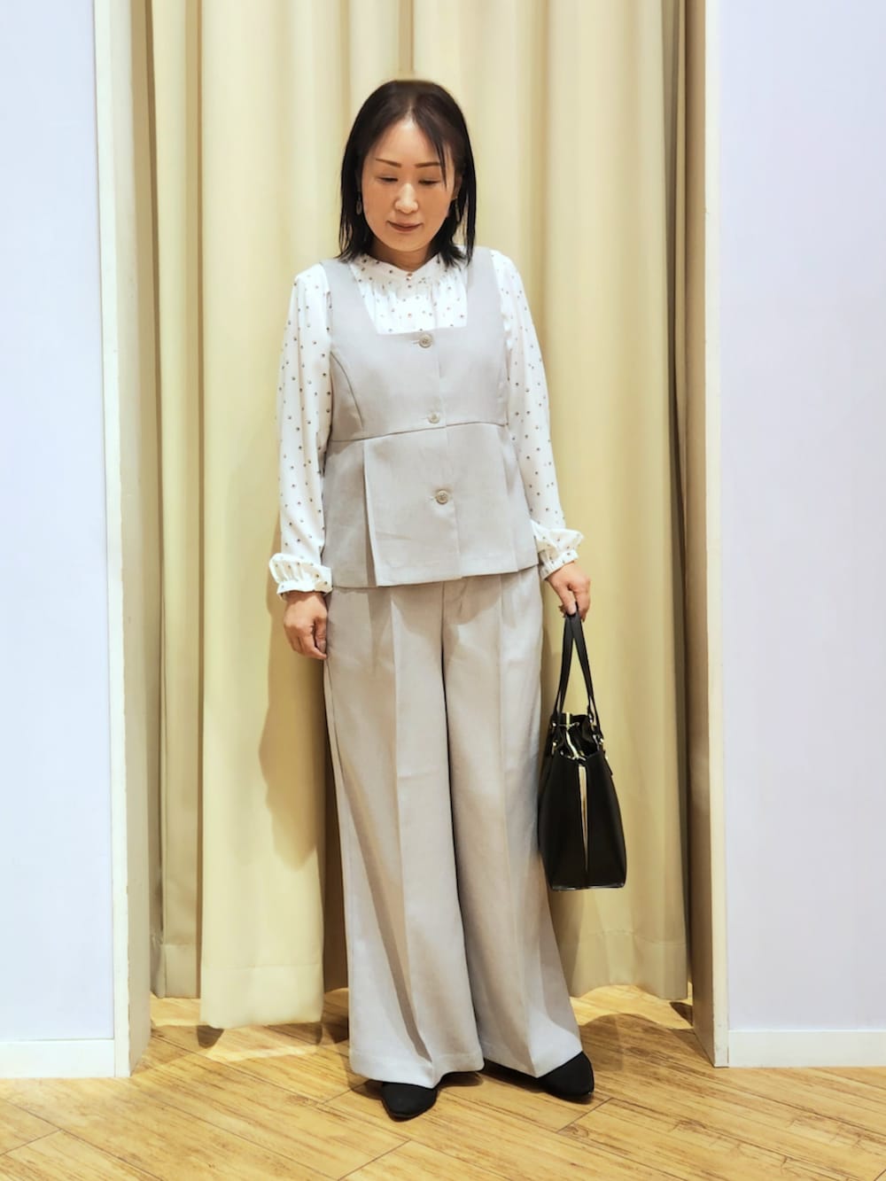 ブラック系のトートバッグ、ブラック系のパンプス、グレー系のパンツドレスを着用したレディースの春コーディネートの4枚目の写真