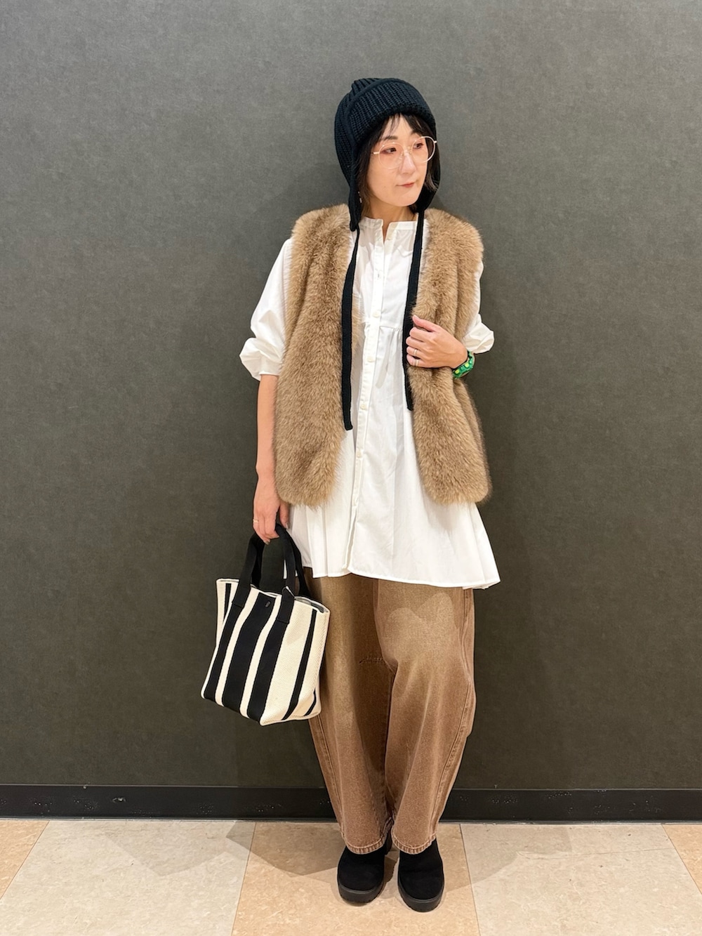 イエロー系のベスト、ホワイト系のチュニック、ブラウン系のデニムパンツを着用したレディースの秋コーディネートの2枚目の写真