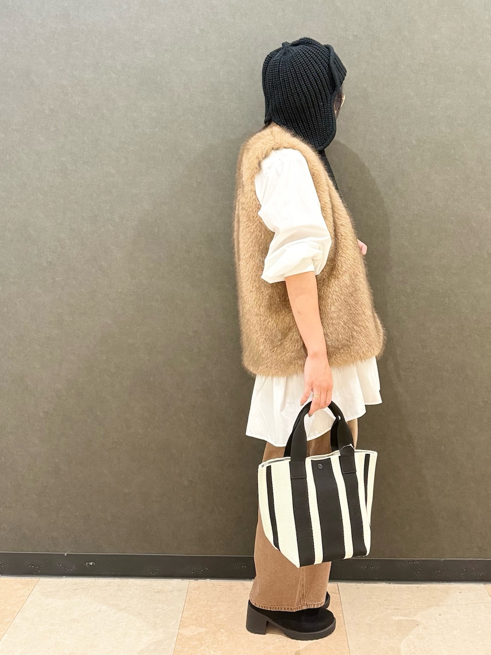 イエロー系のベスト、ホワイト系のチュニック、ブラウン系のデニムパンツを着用したレディースの秋コーディネートの3枚目の写真