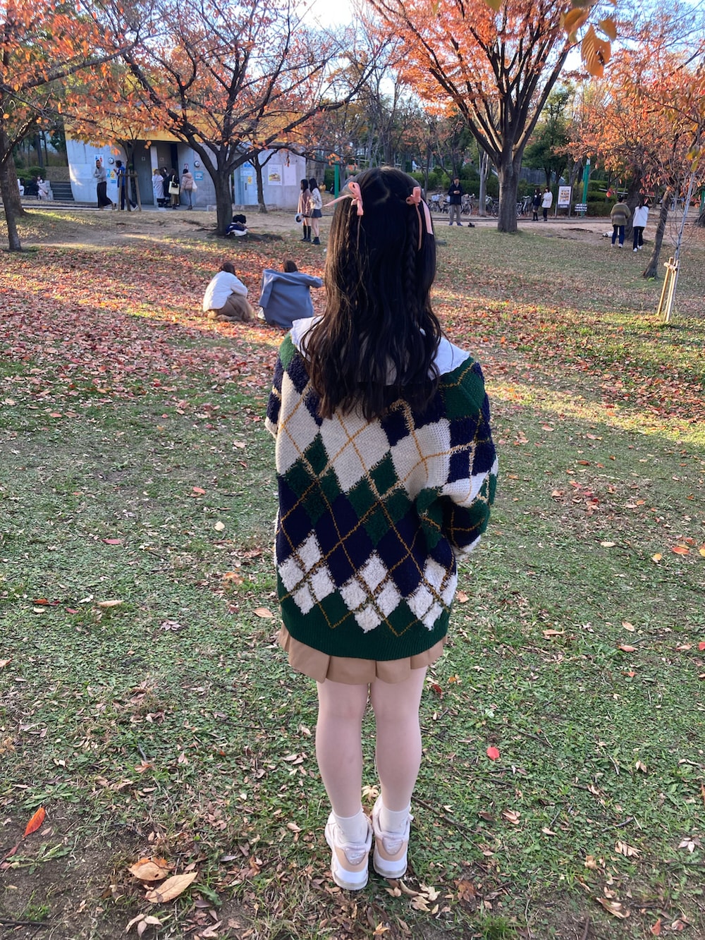 グリーン系のカーディガン/ボレロ、ベージュ系のスカート、ピンク系のスニーカーを着用したレディースの秋コーディネートの2枚目の写真