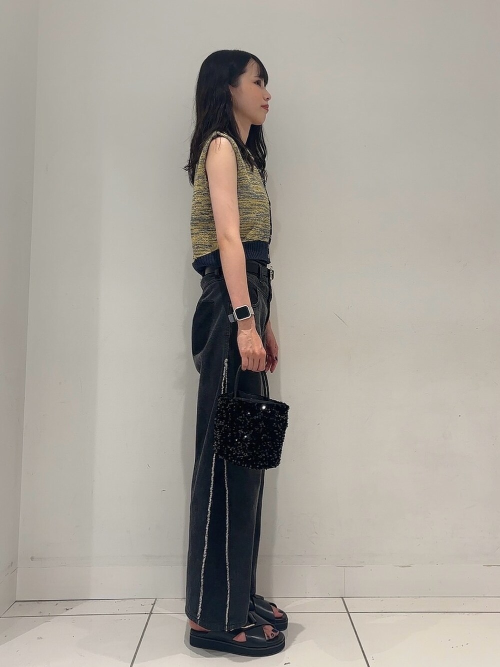 イエロー系のベスト、ブラック系のデニムパンツ、ブラック系のサンダルを着用したレディースの夏コーディネートの2枚目の写真