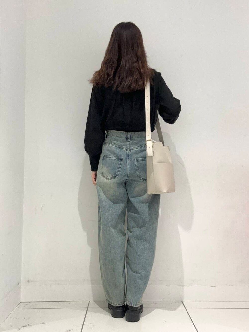 ブルー系のデニムパンツ、ベージュ系のショルダーバッグ、ブラック系のニット/セーターを着用したレディースの秋コーディネートの3枚目の写真