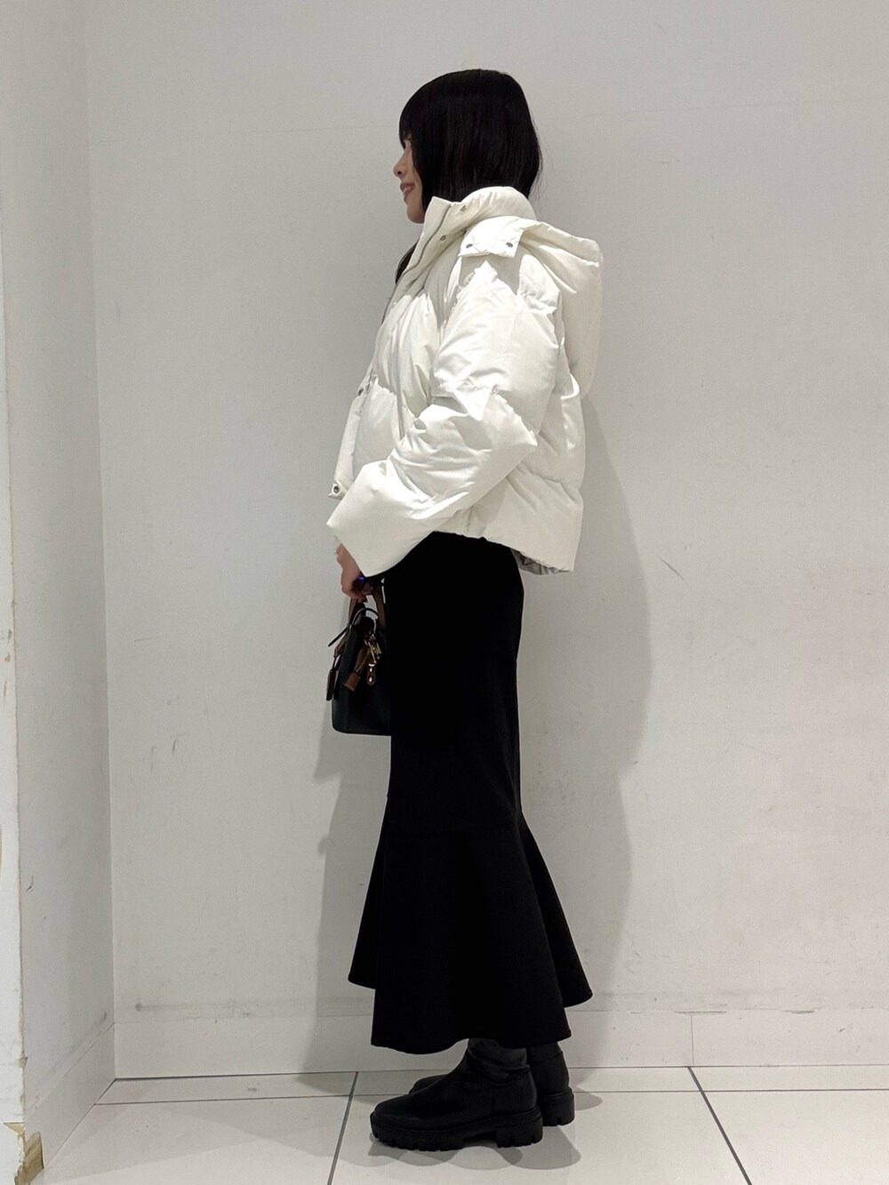 グレー系のニット/セーター、ホワイト系のダウンジャケット/コート、ブラック系のハンドバッグを着用したレディースの冬コーディネートの2枚目の写真