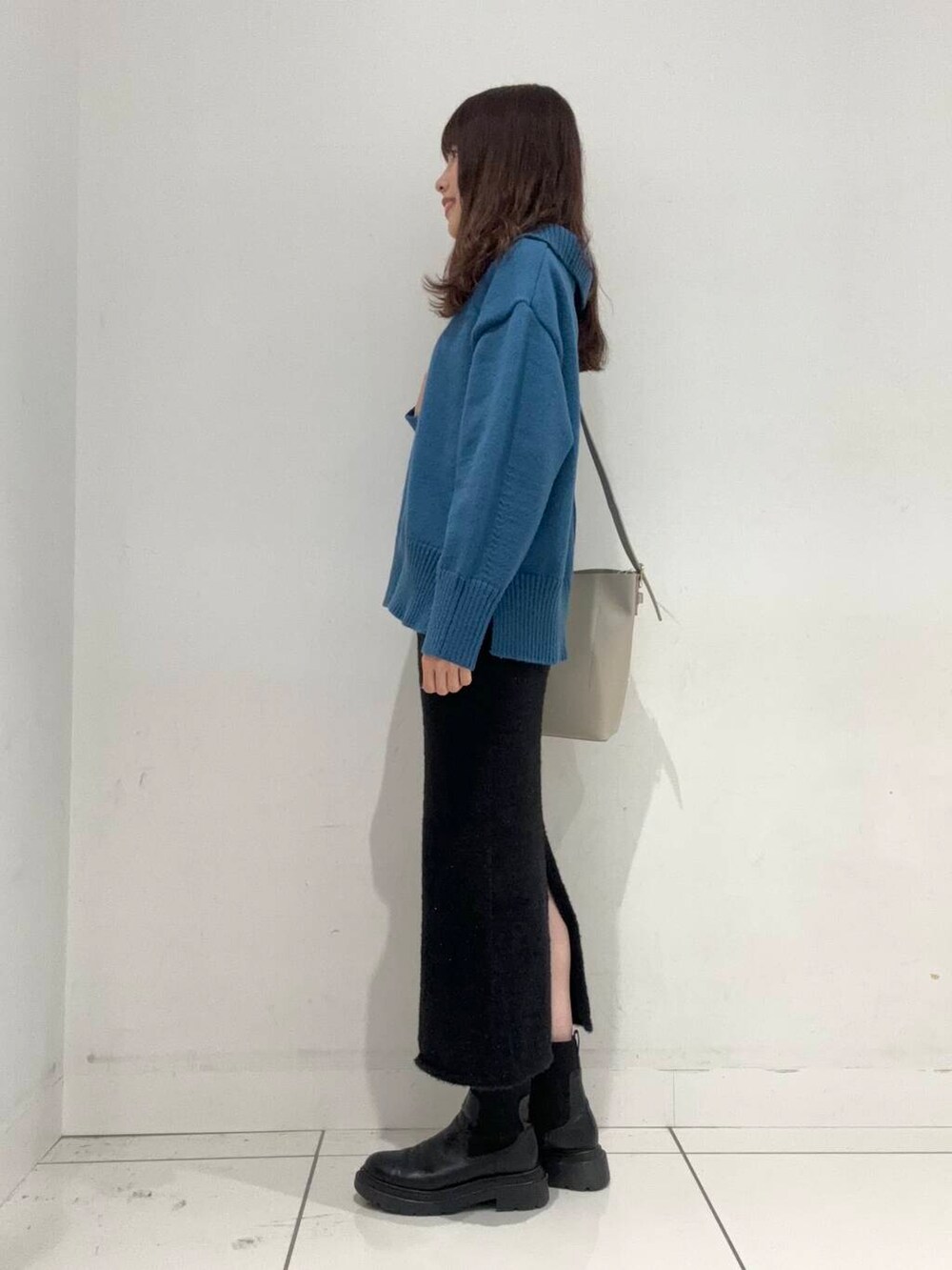 ベージュ系のショルダーバッグ、ブラック系のスカート、ブルー系のニット/セーターを着用したレディースの秋コーディネートの2枚目の写真