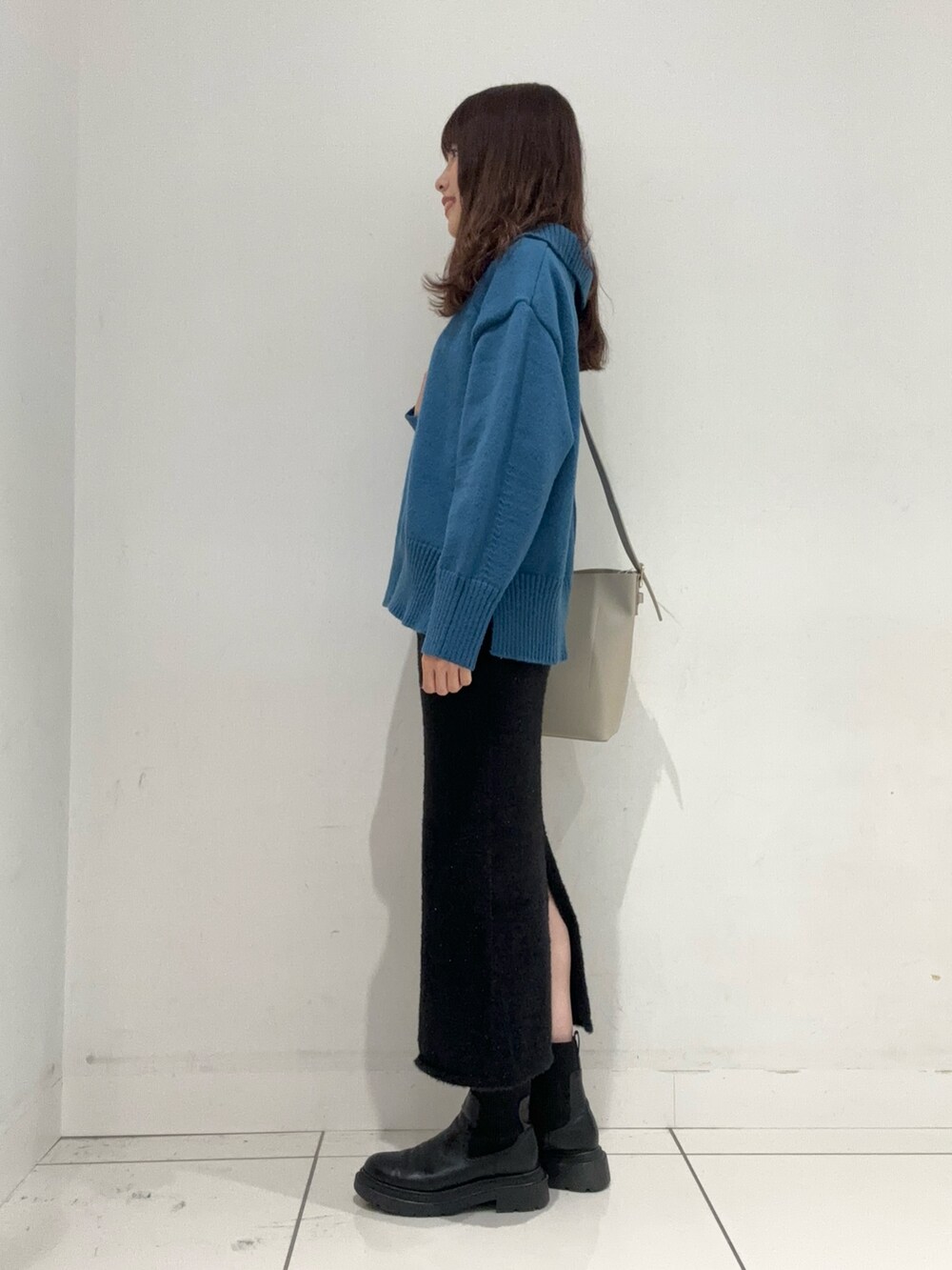 ブルー系のニット/セーター、ブラック系のスカート、ベージュ系のショルダーバッグを着用したレディースの秋コーディネートの2枚目の写真