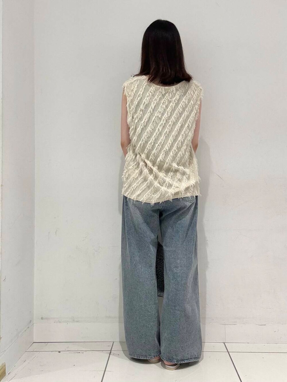 シルバー系のハンドバッグ、ブルー系のデニムパンツ、ブラック系のタンクトップを着用したレディースの夏コーディネートの3枚目の写真