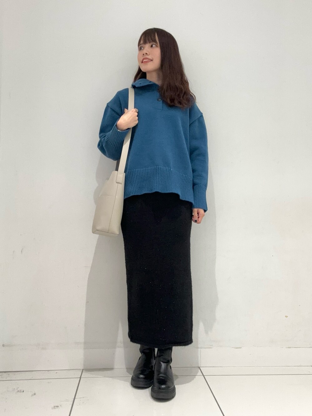 ブルー系のニット/セーター、ブラック系のスカート、ベージュ系のショルダーバッグを着用したレディースの秋コーディネートの4枚目の写真