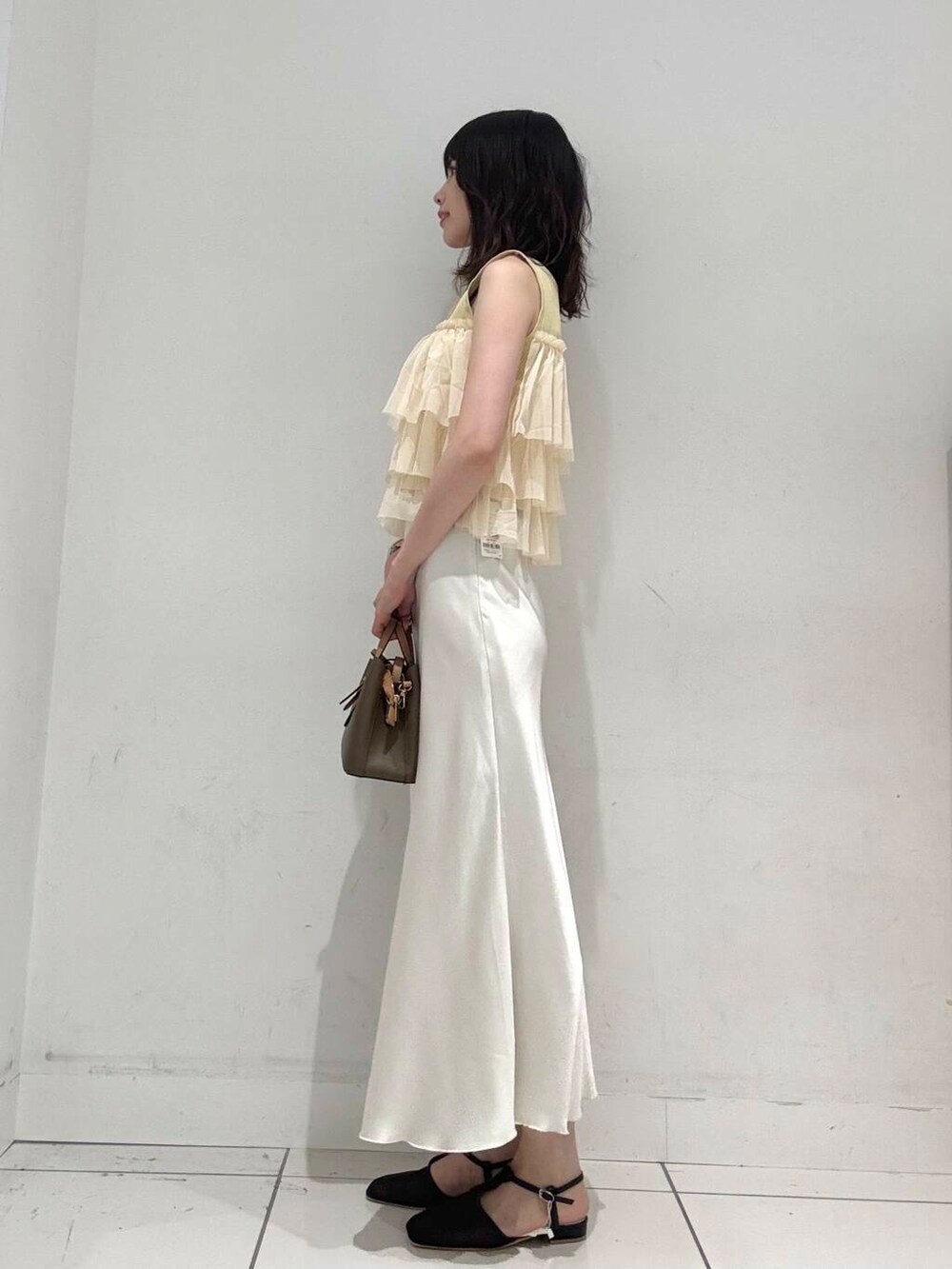 ホワイト系のスカート、ブラウン系のハンドバッグ、ブラック系のパンプスを着用したレディースの夏コーディネートの2枚目の写真