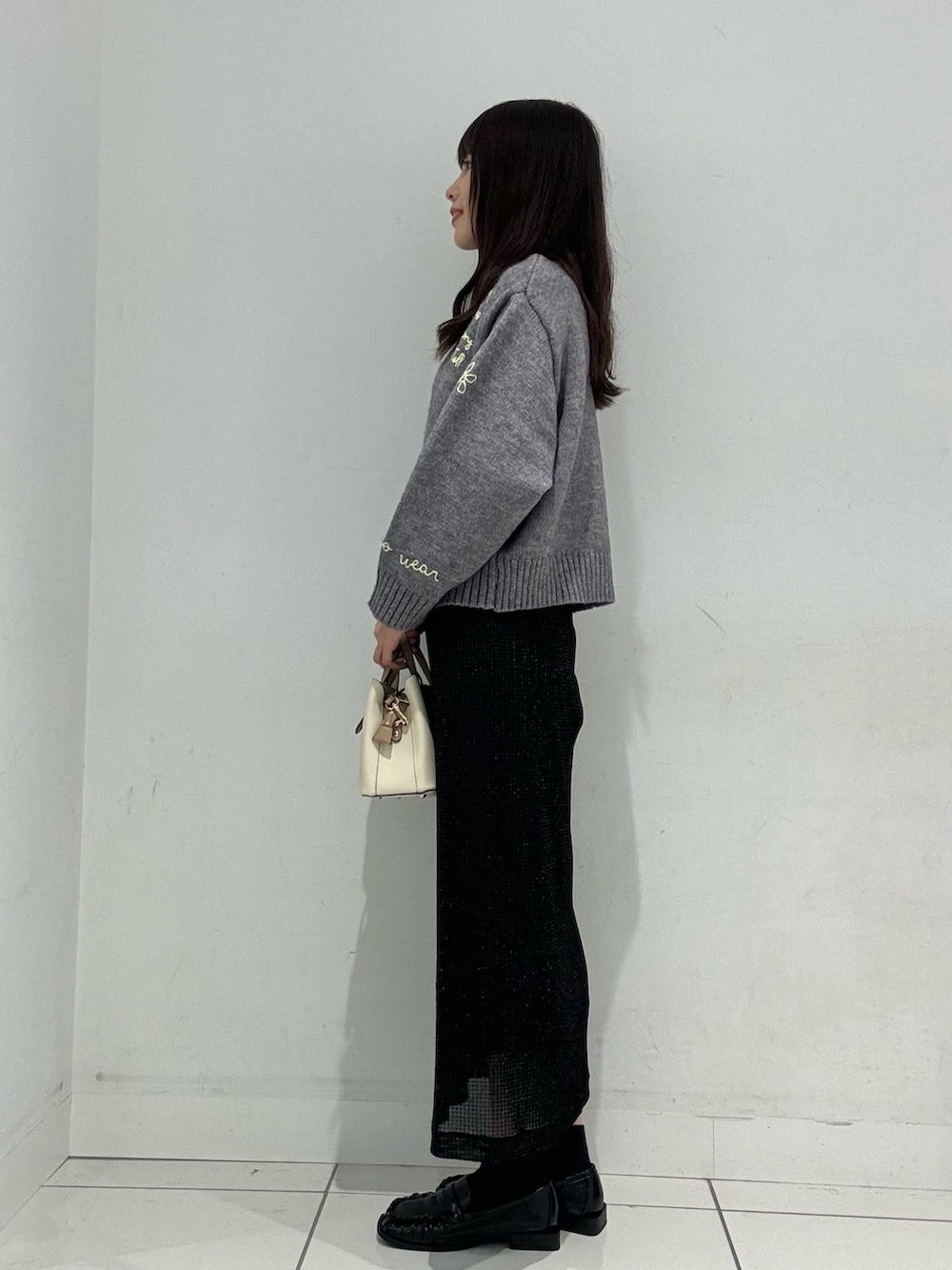グレー系のニット/セーター、ブラック系のローファー、ホワイト系のハンドバッグを着用したレディースの秋コーディネートの2枚目の写真