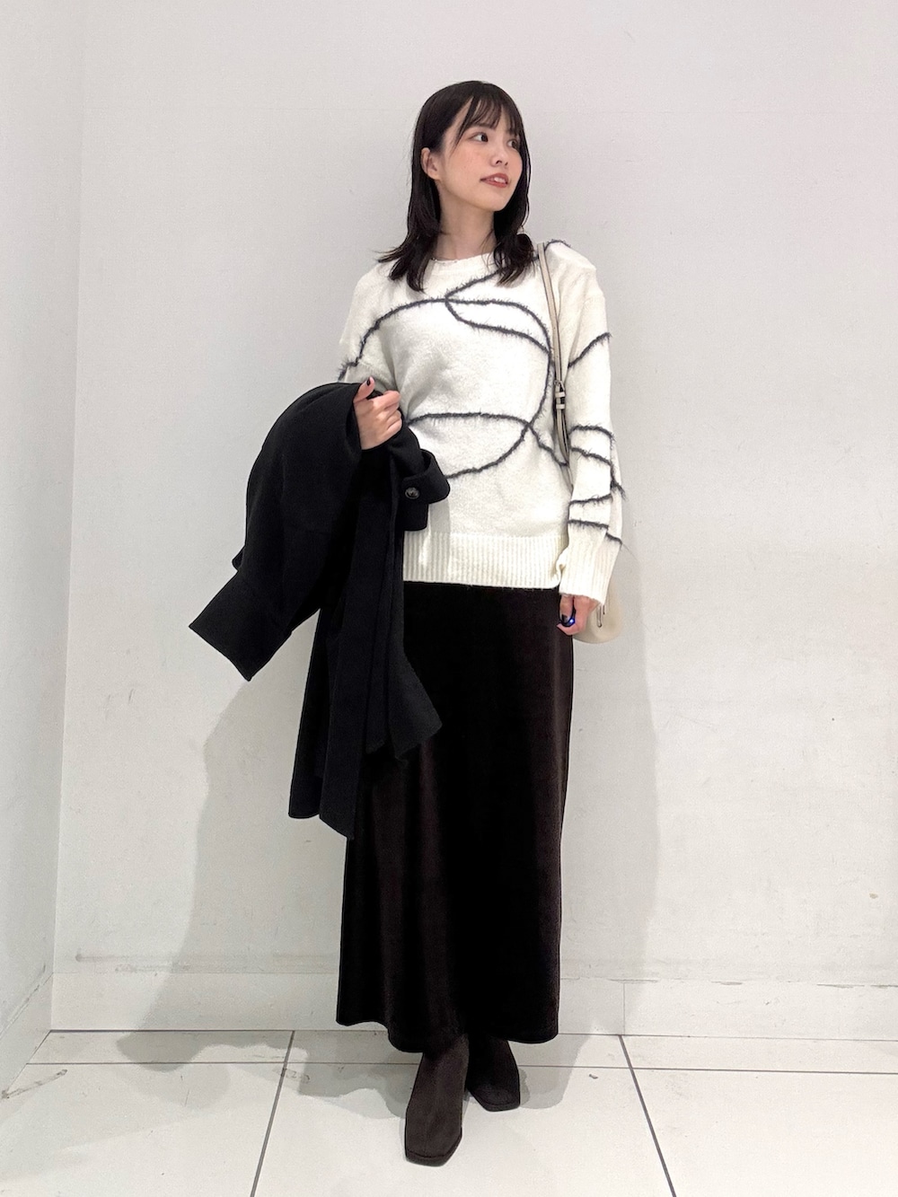 ホワイト系のニット/セーター、ブラウン系のスカート、ブラウン系のブーツを着用したレディースの秋コーディネートの4枚目の写真