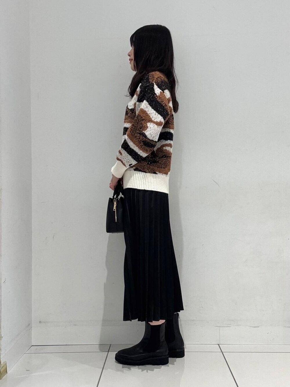 ホワイト系のニット/セーター、ブラック系のブーツ、ブラック系のハンドバッグを着用したレディースの冬コーディネートの2枚目の写真