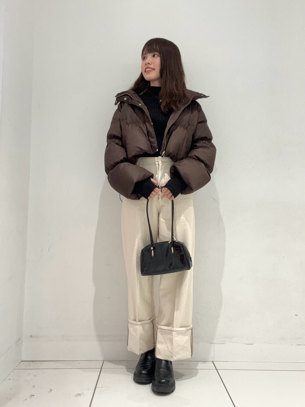 ブラック系のニット/セーター、ブラウン系のダウンジャケット/コート、ホワイト系のデニムパンツを着用したレディースの秋コーディネートの4枚目の写真