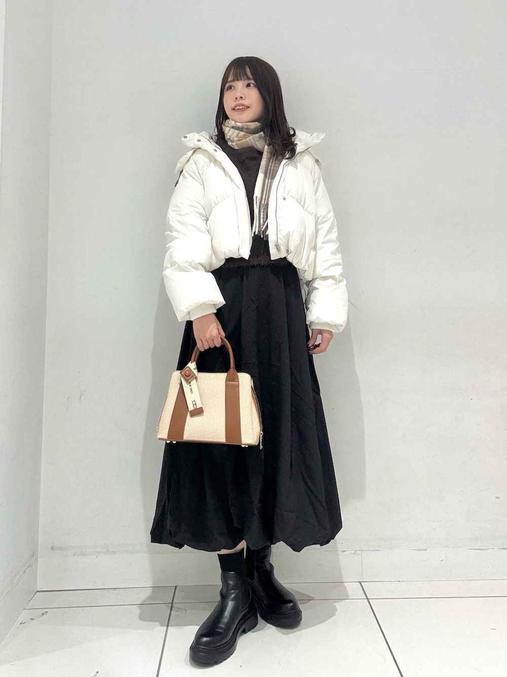 ブラック系のスカート、ブラウン系のニット/セーター、ホワイト系のダウンジャケット/コートを着用したレディースの冬コーディネートの2枚目の写真