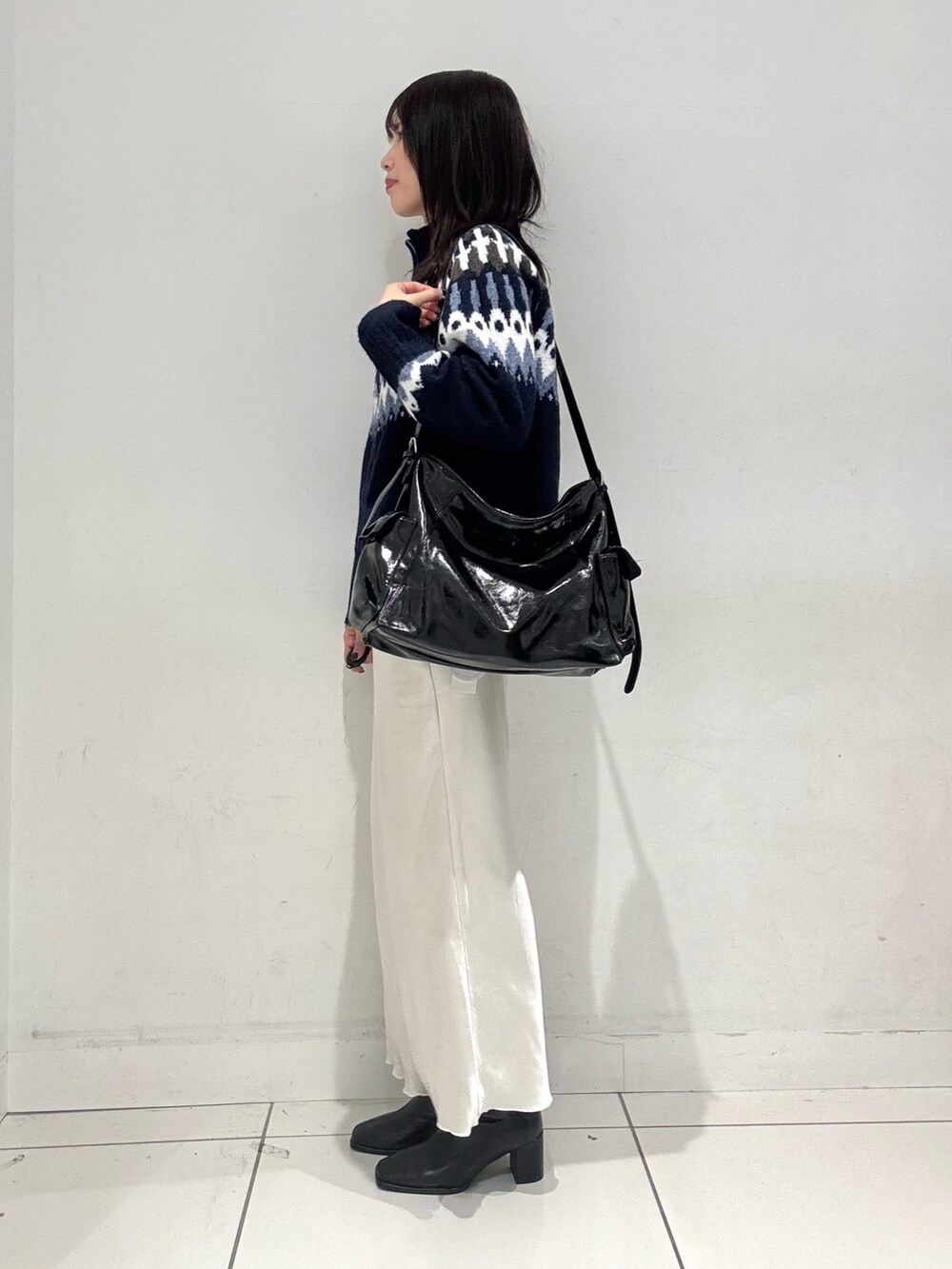 ブルー系のニット/セーター、ホワイト系のスカート、ブラック系のショルダーバッグを着用したレディースの秋コーディネートの2枚目の写真