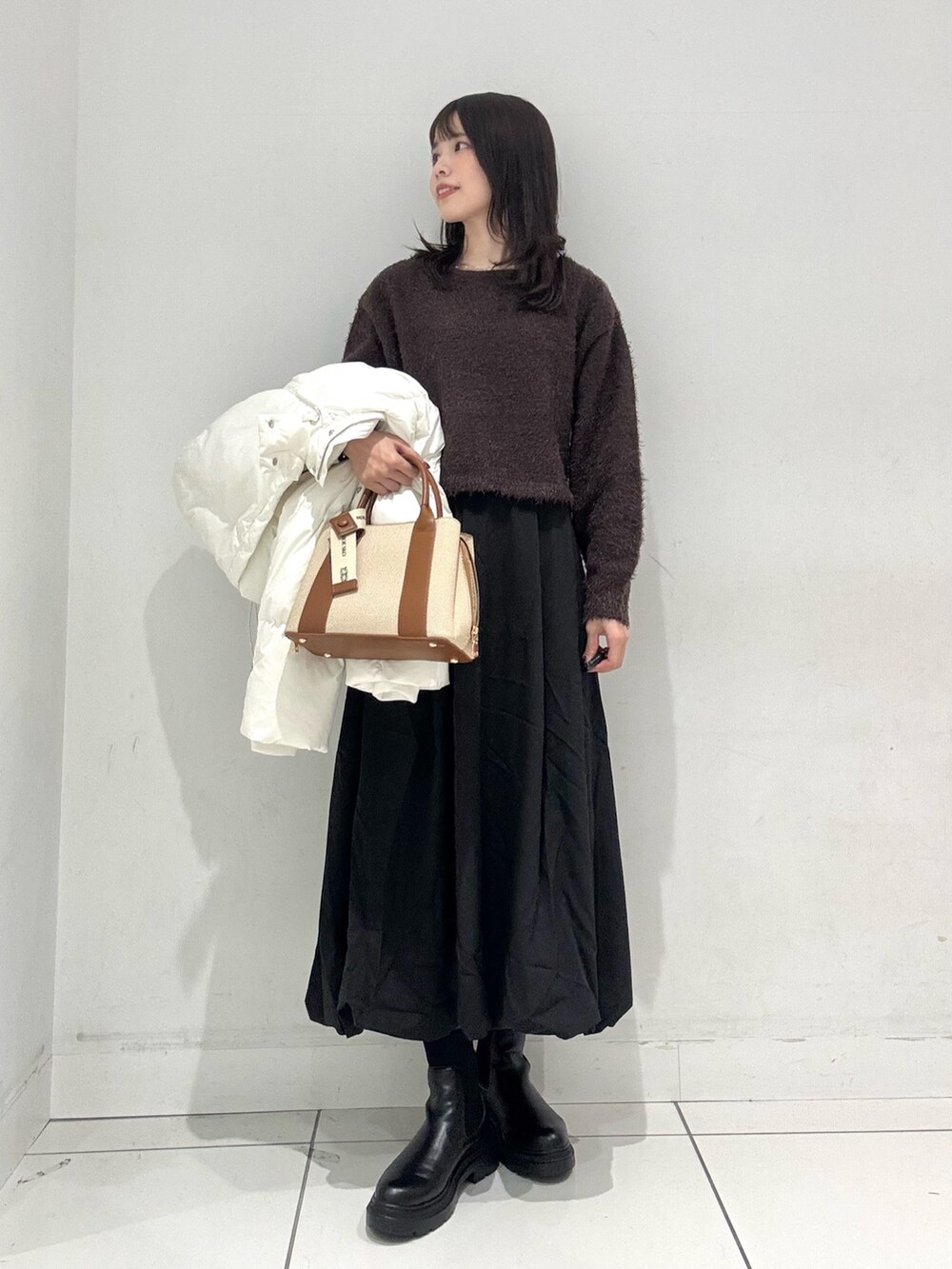 ブラック系のスカート、ブラウン系のニット/セーター、ホワイト系のダウンジャケット/コートを着用したレディースの冬コーディネートの6枚目の写真