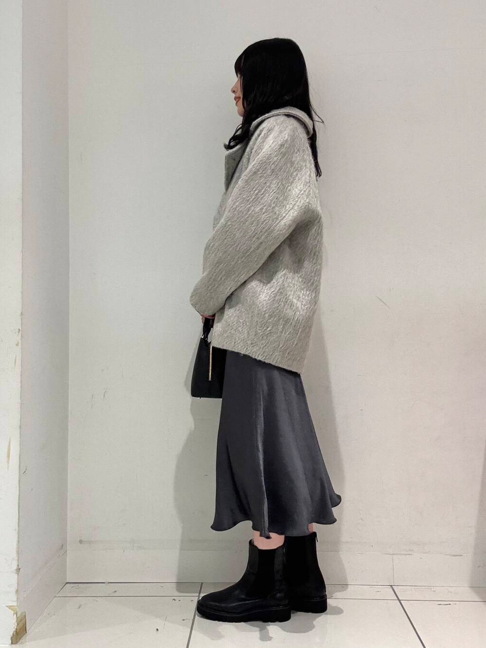 グレー系のスカート、ブラック系のブーツ、ブラック系のハンドバッグを着用したレディースの冬コーディネートの2枚目の写真