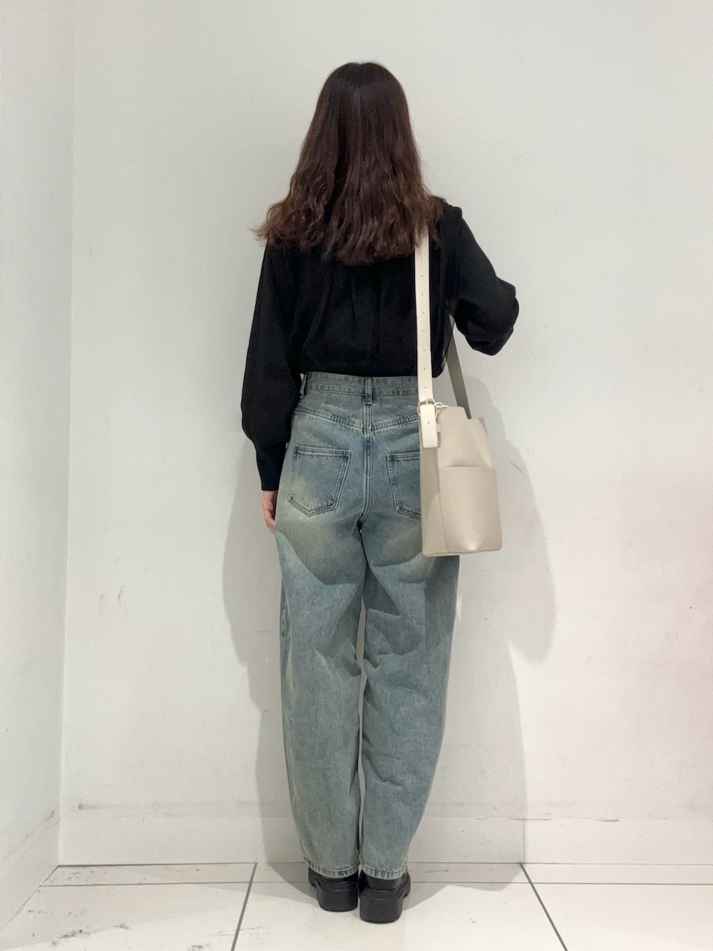 ブルー系のデニムパンツ、ブラック系のニット/セーター、ベージュ系のショルダーバッグを着用したレディースの秋コーディネートの3枚目の写真