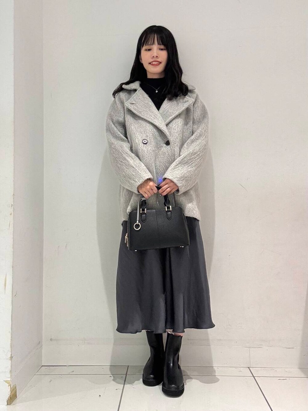 グレー系のスカート、ブラック系のブーツ、ブラック系のハンドバッグを着用したレディースの冬コーディネートの4枚目の写真