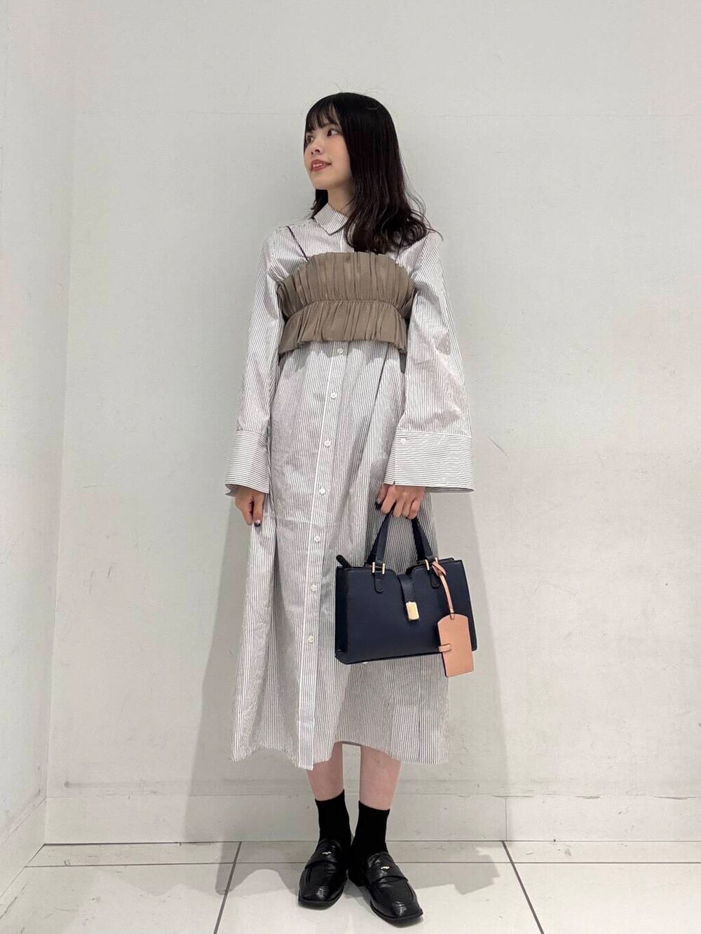 ブルー系のハンドバッグ、ブラック系のローファー、ベージュ系のワンピースを着用したレディースの春コーディネートの4枚目の写真