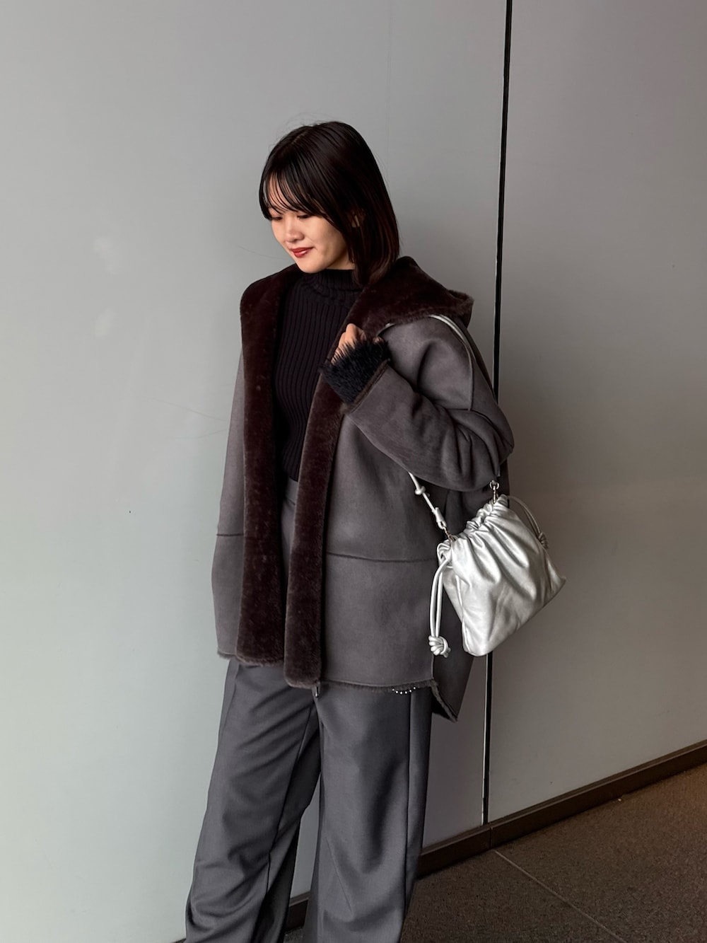 グレー系のスラックス、シルバー系のショルダーバッグ、グレー系のムートンコートを着用したレディースの秋コーディネートの6枚目の写真