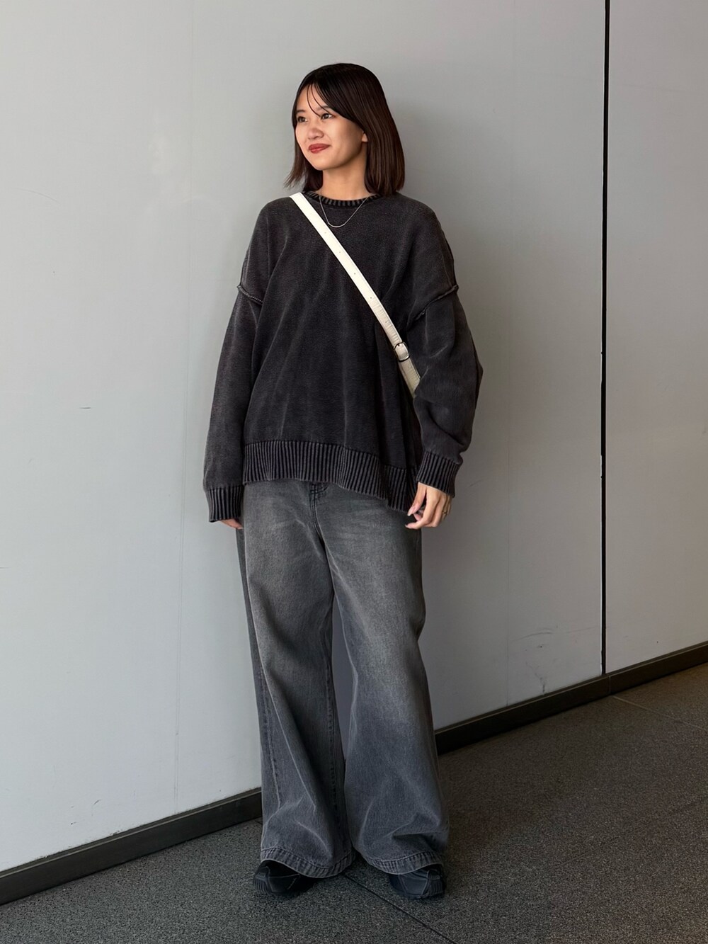 ブラック系のデニムパンツ、ブラック系のニット/セーター、ホワイト系のショルダーバッグを着用したレディースの秋コーディネートの2枚目の写真