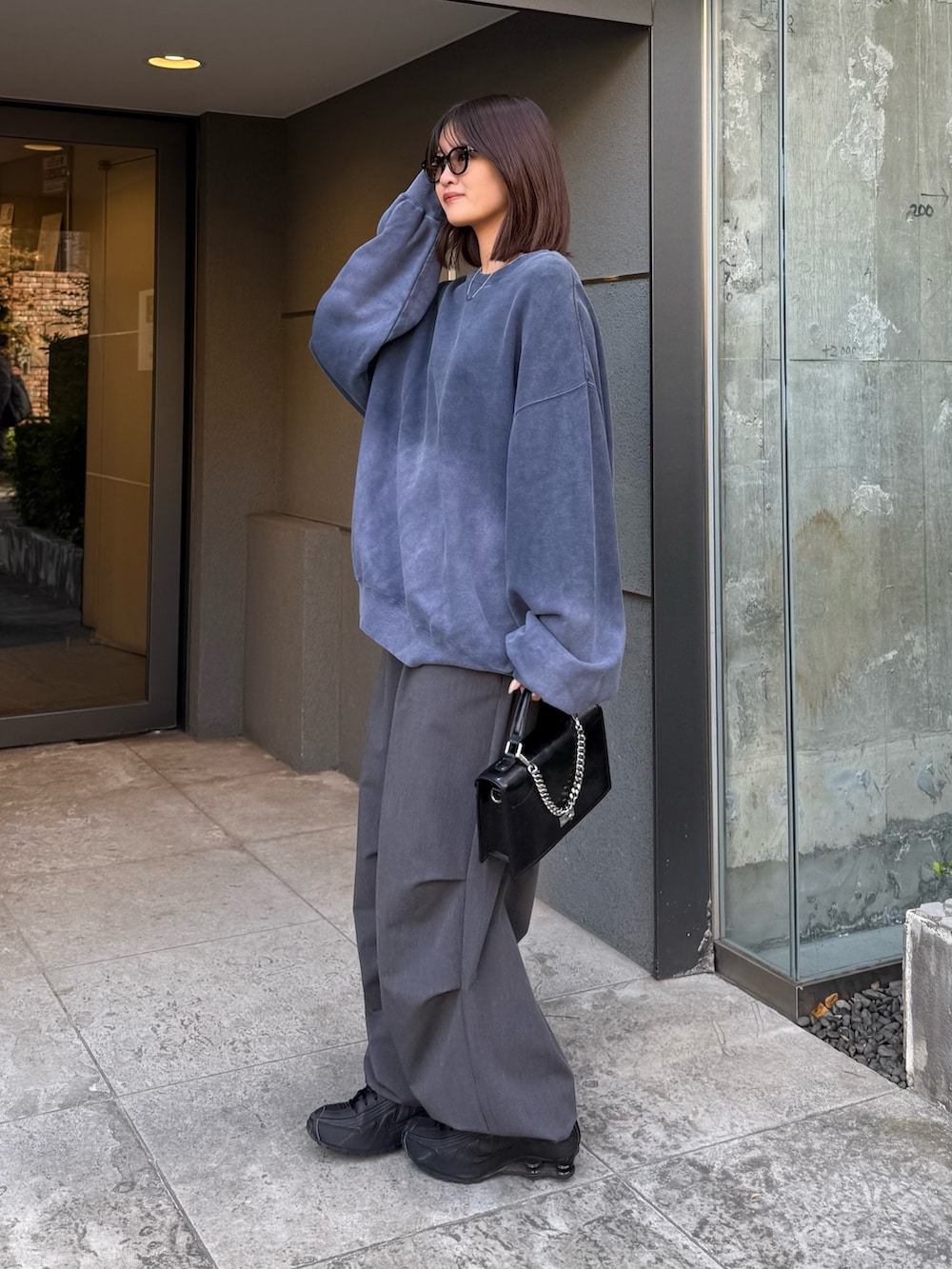 ブルー系のスウェット、ブラック系のショルダーバッグ、グレー系のスラックスを着用したレディースの冬コーディネートの2枚目の写真