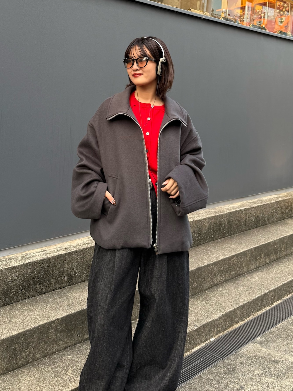 グレー系のブルゾン、レッド系のカーディガン/ボレロ、ブラック系のデニムパンツを着用したレディースの秋コーディネートの6枚目の写真