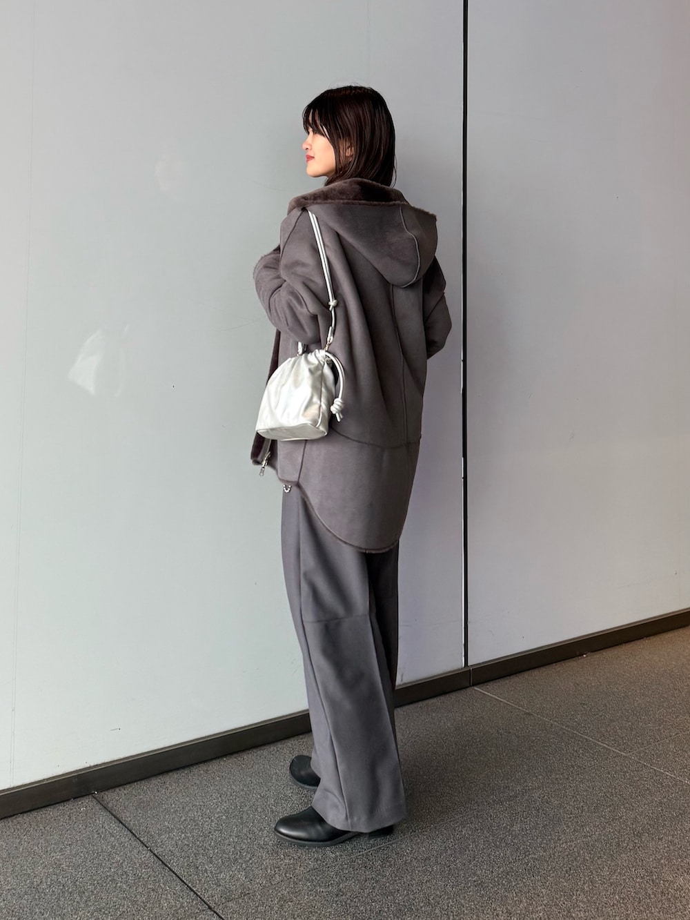 グレー系のスラックス、シルバー系のショルダーバッグ、グレー系のムートンコートを着用したレディースの秋コーディネートの3枚目の写真