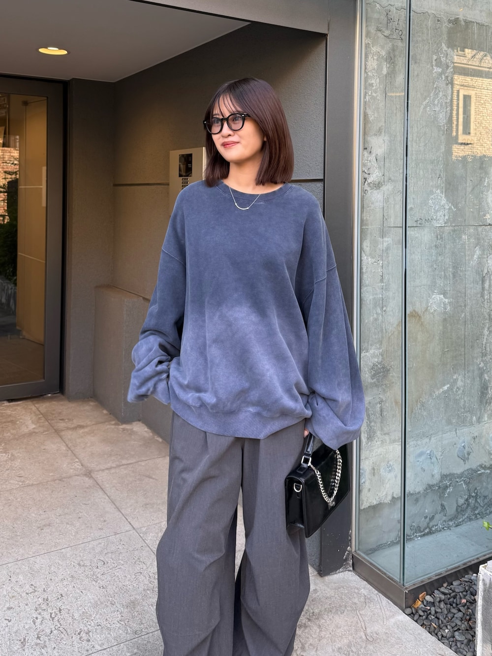 ブルー系のスウェット、ブラック系のショルダーバッグ、グレー系のスラックスを着用したレディースの冬コーディネートの3枚目の写真