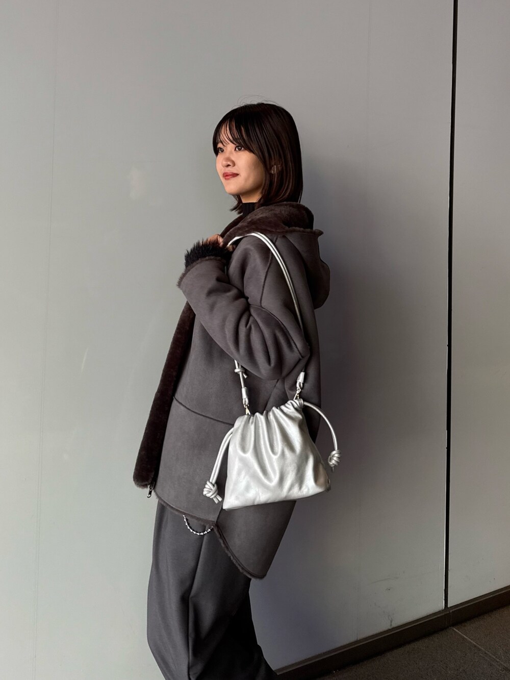グレー系のスラックス、シルバー系のショルダーバッグ、グレー系のムートンコートを着用したレディースの秋コーディネートの7枚目の写真