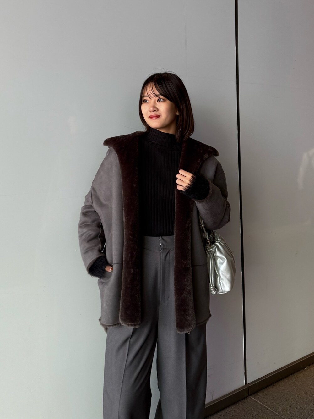 グレー系のスラックス、シルバー系のショルダーバッグ、グレー系のムートンコートを着用したレディースの秋コーディネートの5枚目の写真