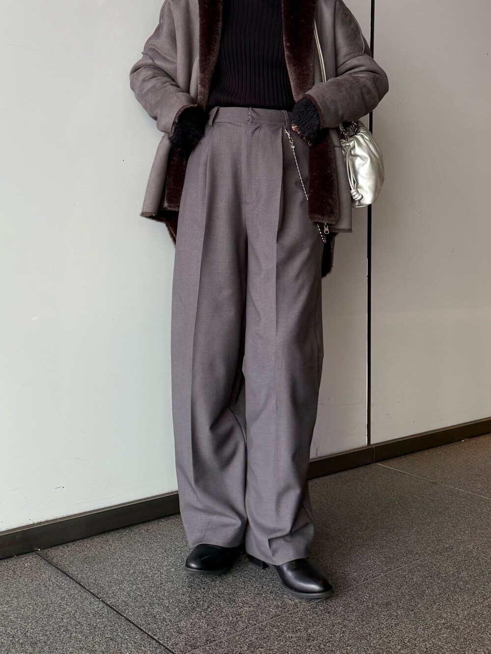 グレー系のスラックス、シルバー系のショルダーバッグ、グレー系のムートンコートを着用したレディースの秋コーディネートの9枚目の写真