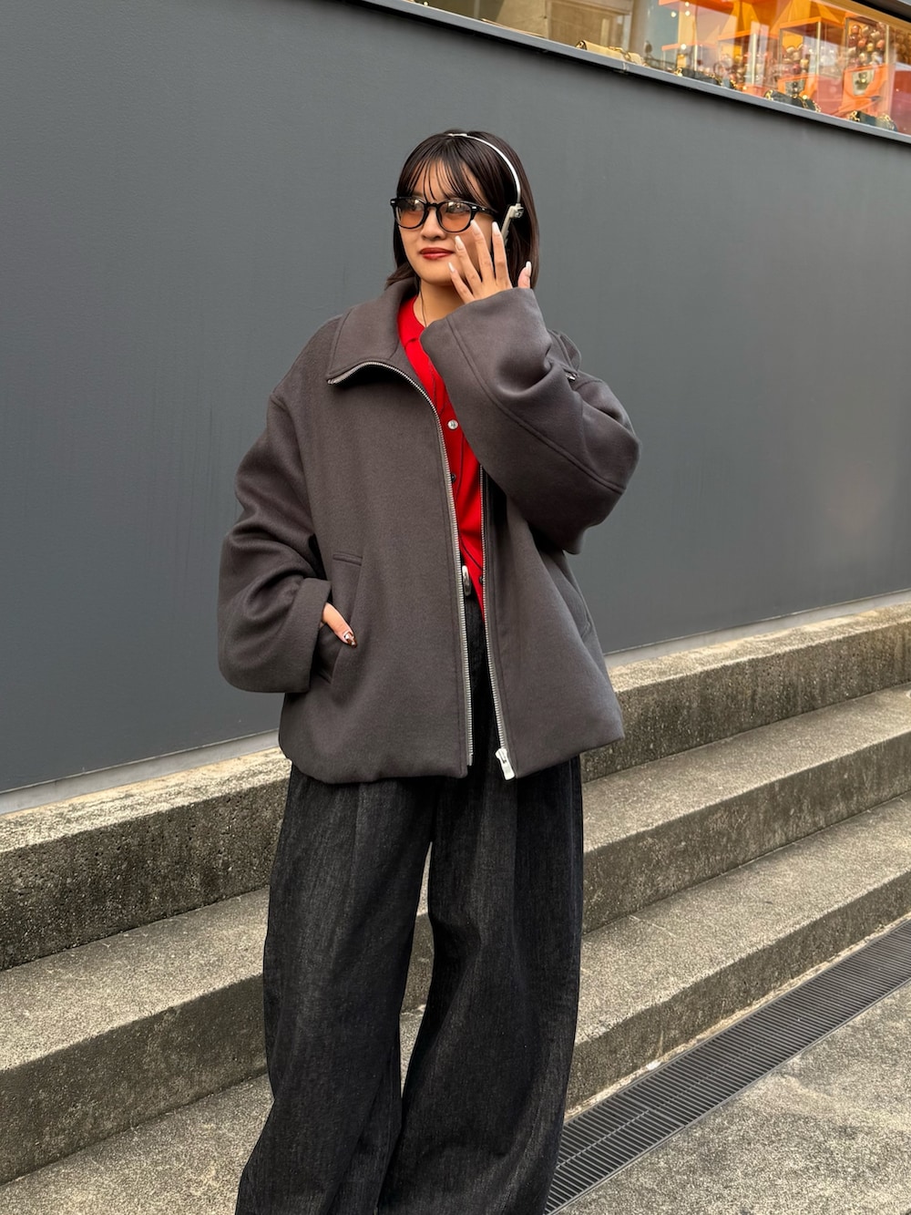 グレー系のブルゾン、レッド系のカーディガン/ボレロ、ブラック系のデニムパンツを着用したレディースの秋コーディネートの3枚目の写真