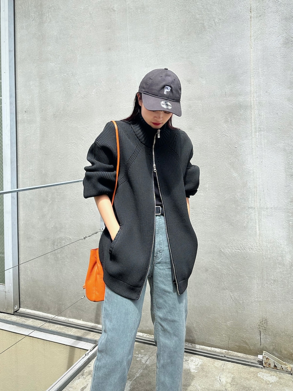 ブラック系のニット/セーター、オレンジ系のショルダーバッグ、グレー系のデニムパンツを着用したレディースの秋コーディネートの2枚目の写真