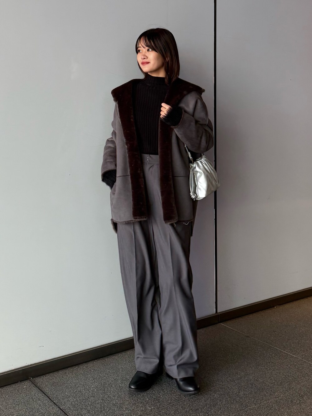 グレー系のスラックス、シルバー系のショルダーバッグ、グレー系のムートンコートを着用したレディースの秋コーディネートの2枚目の写真