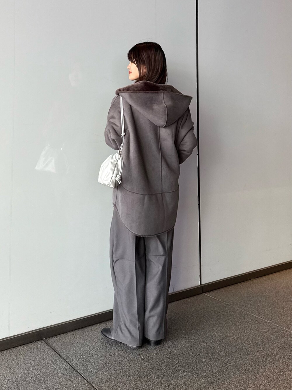 グレー系のスラックス、シルバー系のショルダーバッグ、グレー系のムートンコートを着用したレディースの秋コーディネートの4枚目の写真