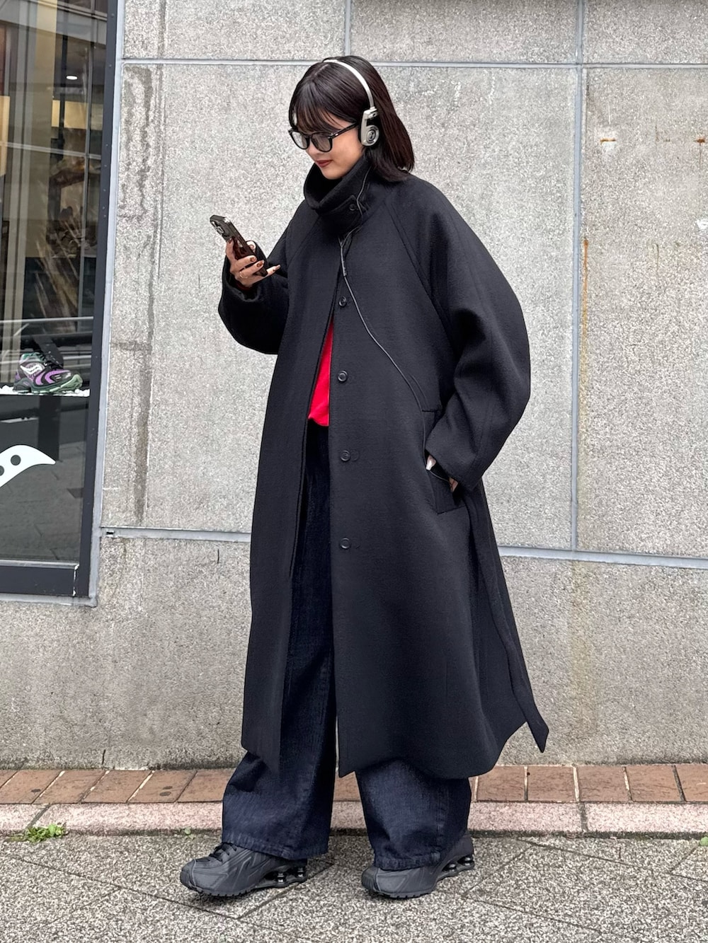 ブラック系のステンカラーコート、ブルー系のデニムパンツ、ブラック系のサングラスを着用したレディースの秋コーディネートの2枚目の写真