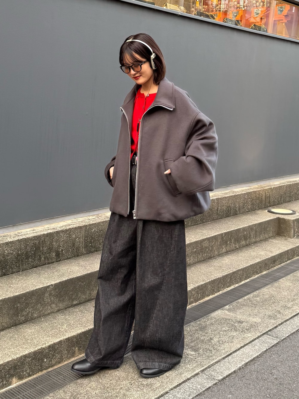 グレー系のブルゾン、レッド系のカーディガン/ボレロ、ブラック系のデニムパンツを着用したレディースの秋コーディネートの2枚目の写真