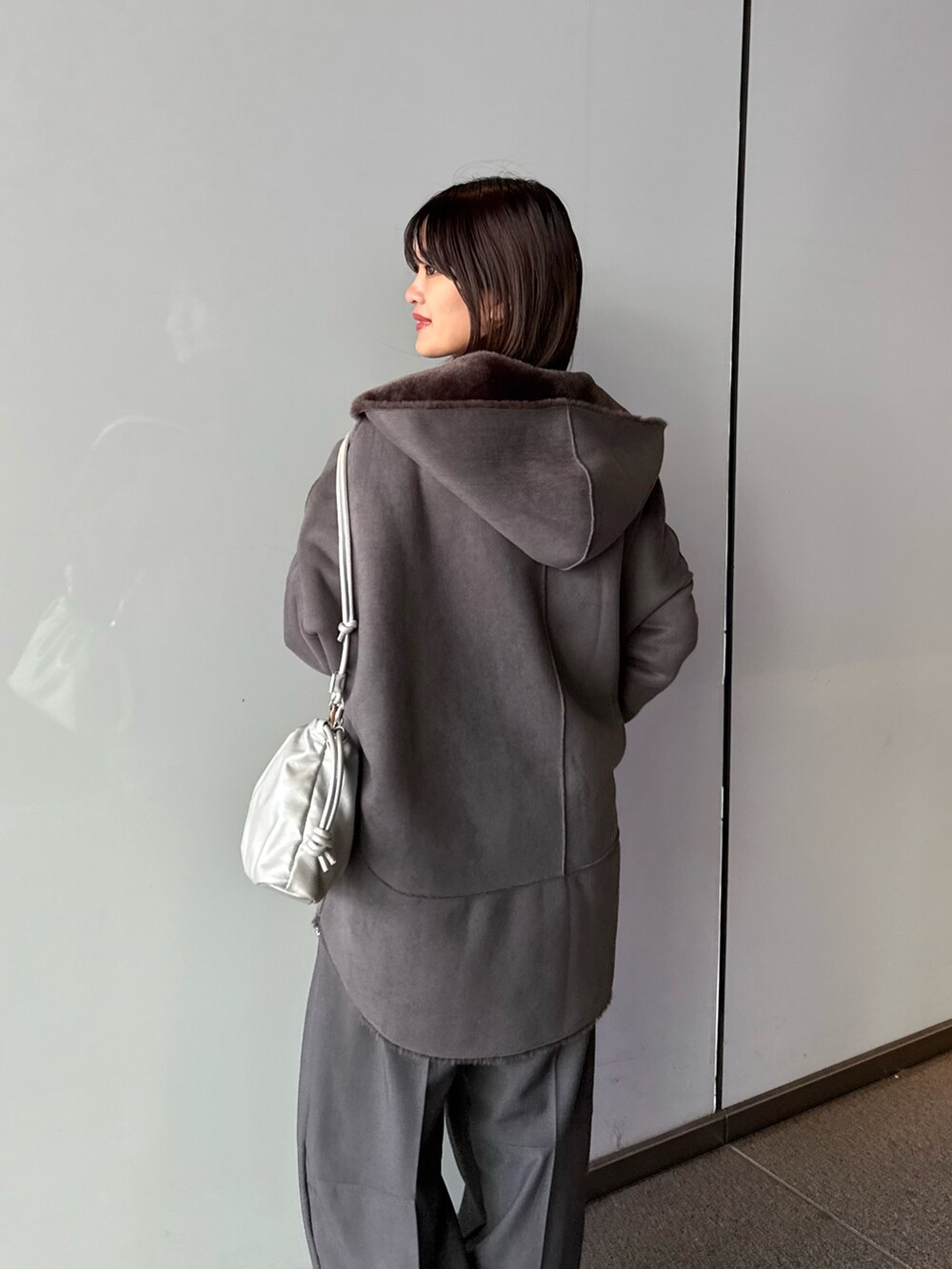 グレー系のスラックス、シルバー系のショルダーバッグ、グレー系のムートンコートを着用したレディースの秋コーディネートの8枚目の写真