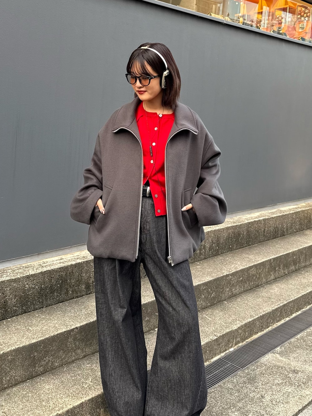 グレー系のブルゾン、レッド系のカーディガン/ボレロ、ブラック系のデニムパンツを着用したレディースの秋コーディネートの4枚目の写真