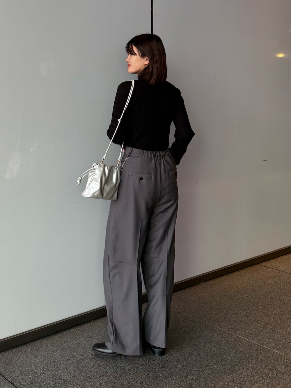 グレー系のスラックス、シルバー系のショルダーバッグ、ブラック系のTシャツ/カットソーを着用したレディースの秋コーディネートの3枚目の写真