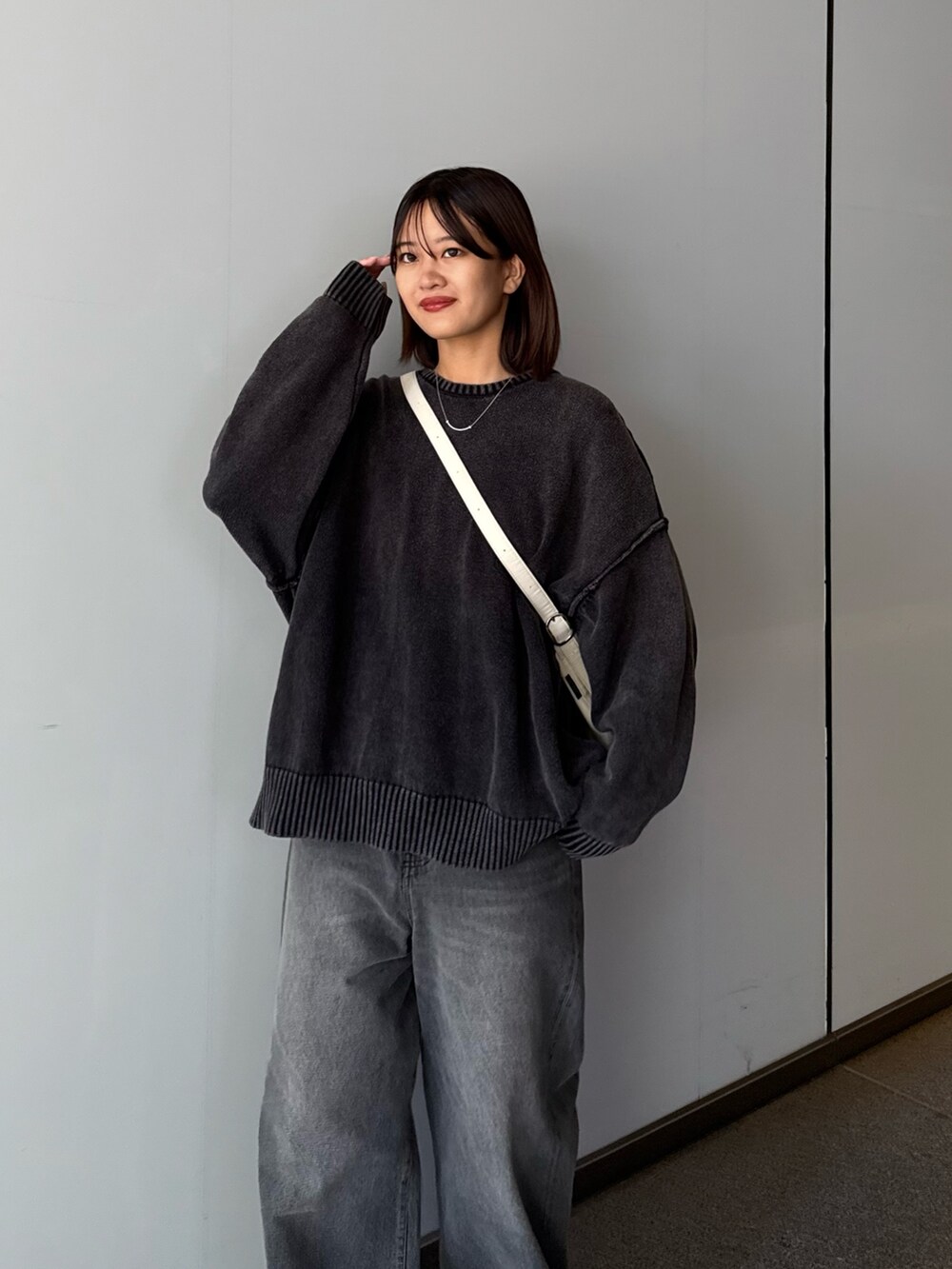 ブラック系のデニムパンツ、ブラック系のニット/セーター、ホワイト系のショルダーバッグを着用したレディースの秋コーディネートの4枚目の写真